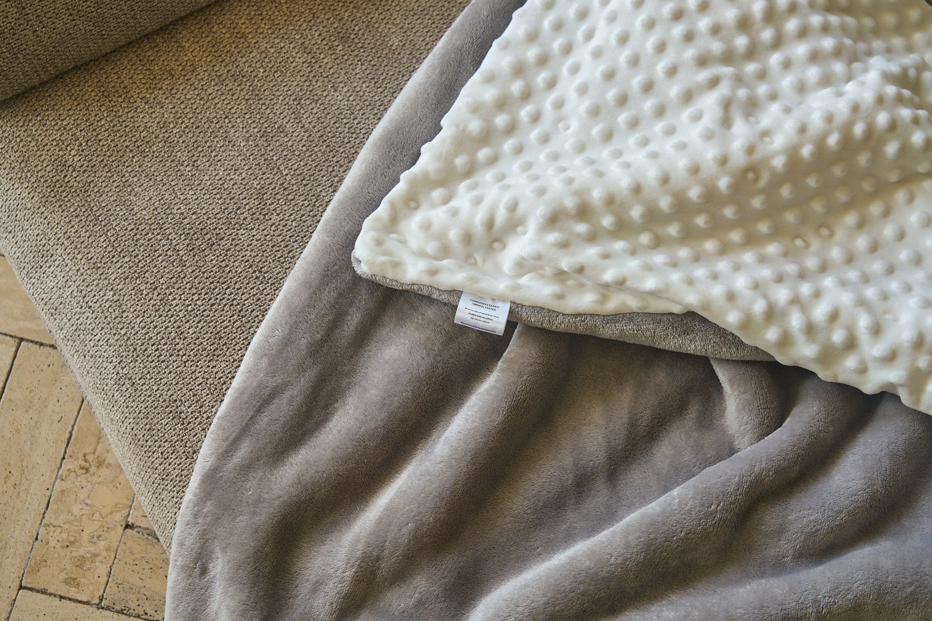 Close-up of comfort blanket corner: gray fabric with white textured dots and label