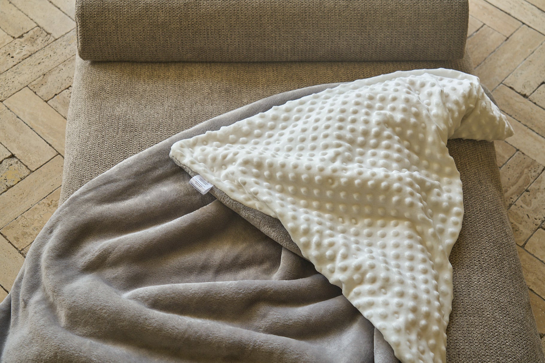 Comfort blanket on sofa armrest; taupe and gray fabric with white bumpy panel