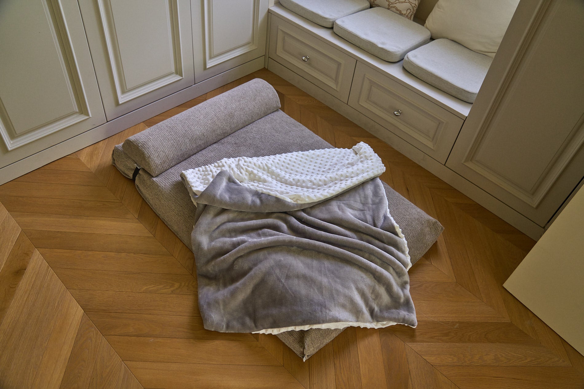 Comfort blanket draped on a beige sofa bed; gray underside with white textured top