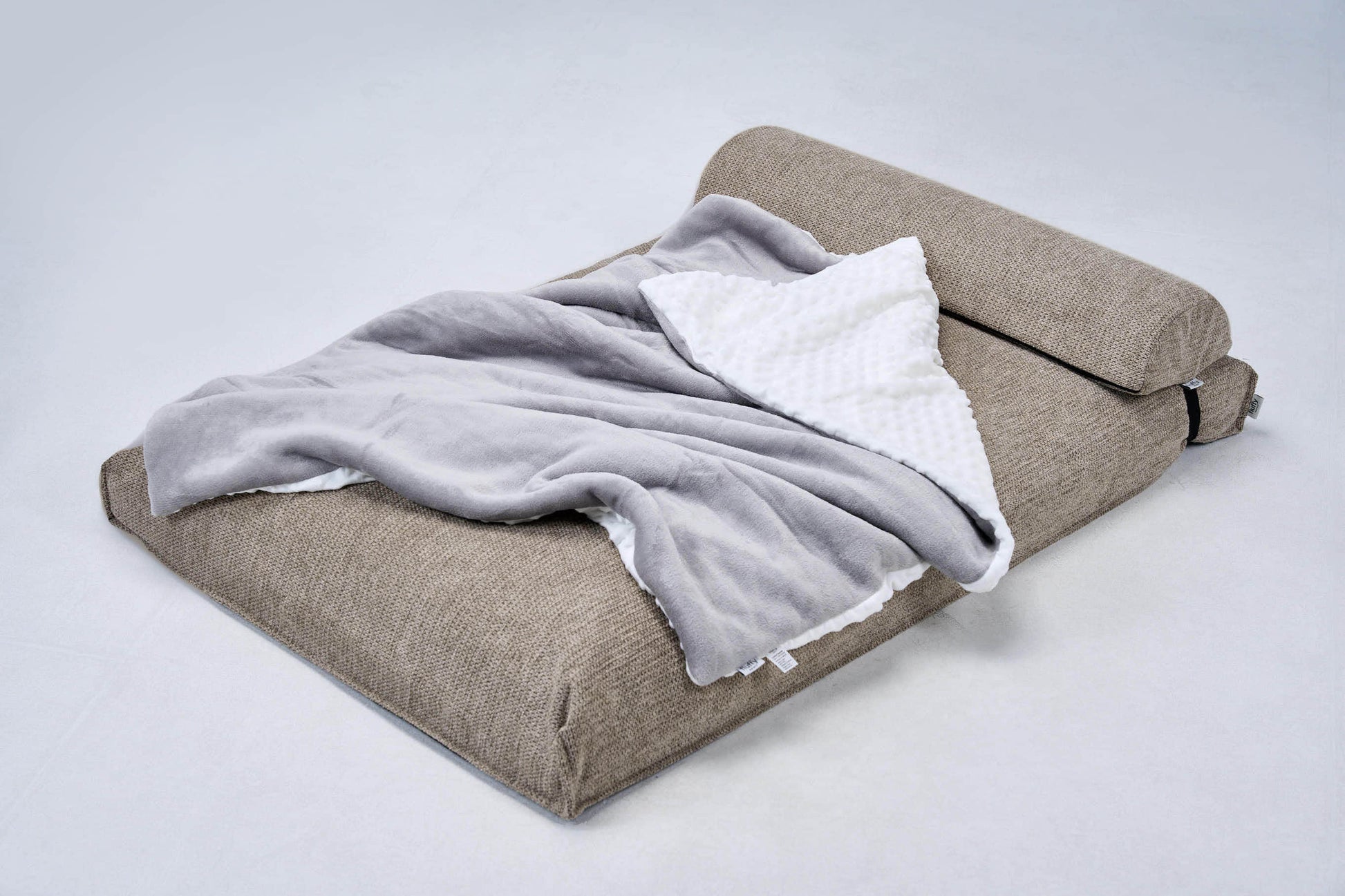 AirNest pillow with anthracite-gray cover, stacked with a light blanket on top