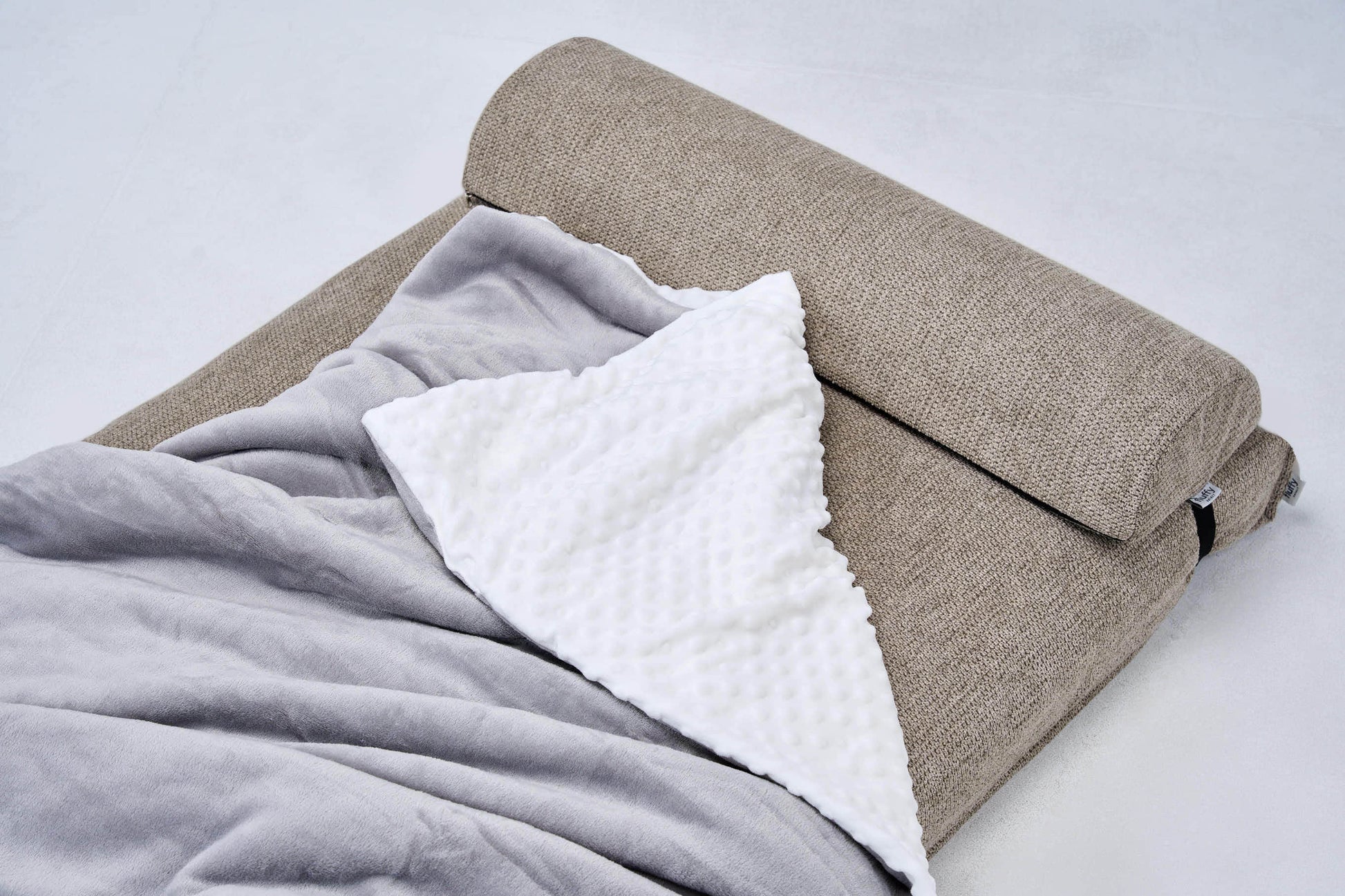 Dog bed with beige cover and white and gray blankets tucked on top